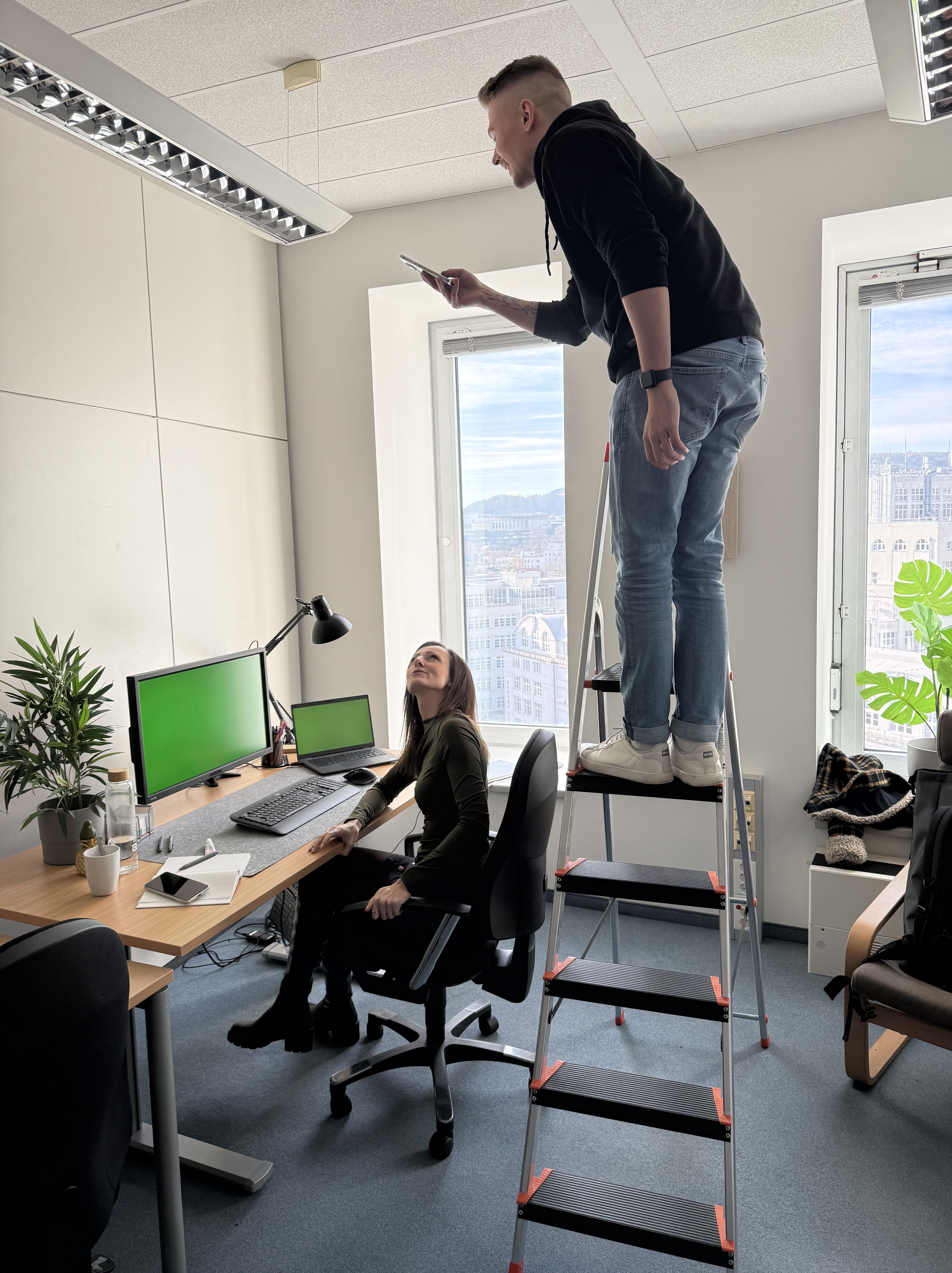 Kollege macht Foto von Corporate Influencerin von einer Leiter aus