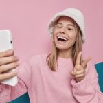 Junge, blonde Frau macht ein Selfie und zeigt das Peace-Zeichen mit der Hand