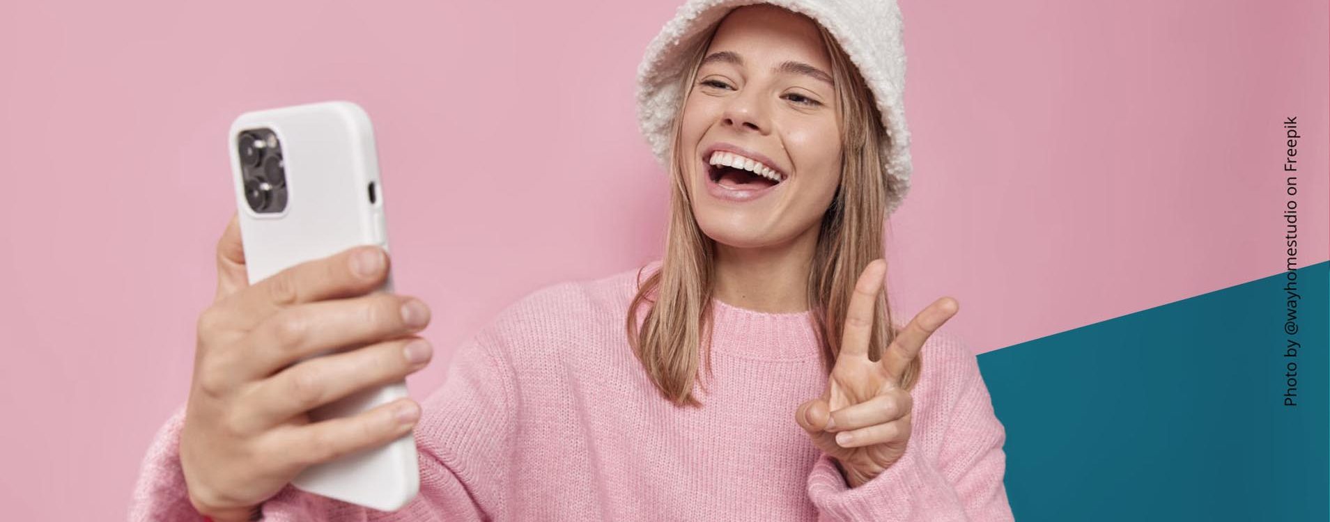 Junge, blonde Frau macht ein Selfie und zeigt das Peace-Zeichen mit der Hand