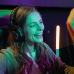 Junge Frau spielt ein Videospiel, trägt Kopfhörer und lacht