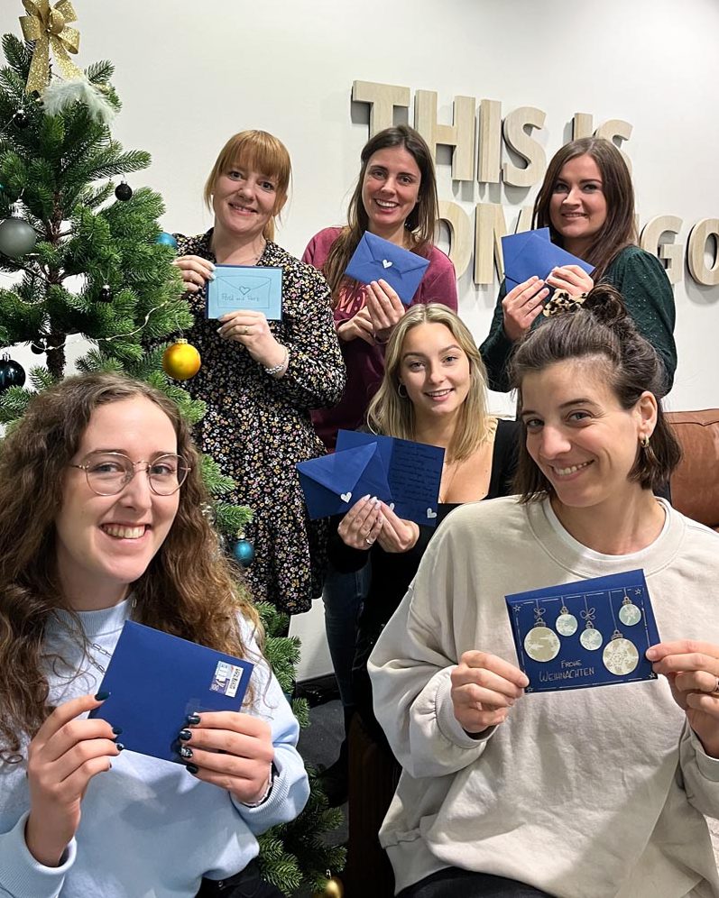 Sechs Frauen posieren vor einem Weihnachtsbaum mit selbst gebastelten Weihnachtskarten