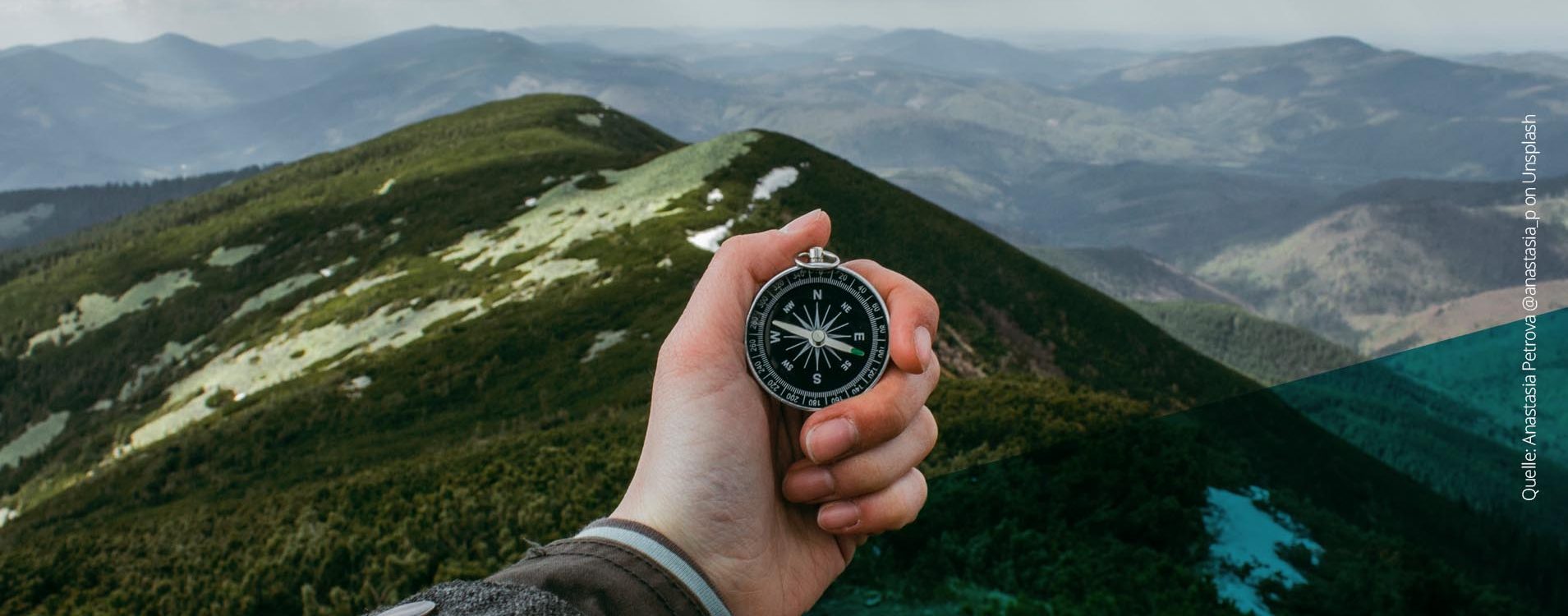 Hand mit Kompass schaut von einem Berg in die Ferne