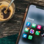 Handy auf einem Tisch mit einigen Social Media Apps auf dem Bildschirm, daneben eine Kaffeetasse