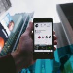 Hand hält ein Handy in die Luft, Hochhäuser im Hintergrund