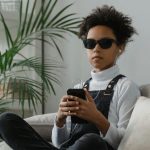 Blinde Frau sitzt auf Couch, hat ein Smartphone in der Hand und angeschlossene Kopfhörer in den Ohren, sie lässt sich etwas per Screenreader vorlesen, was für Barrierefreiheit in Social Media steht