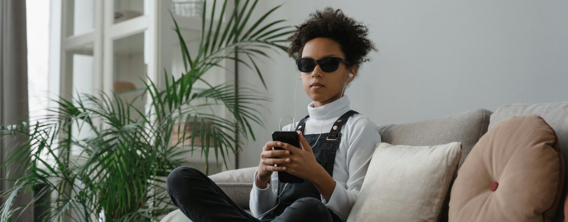 Blinde Frau sitzt auf Couch, hat ein Smartphone in der Hand und angeschlossene Kopfhörer in den Ohren, sie lässt sich etwas per Screenreader vorlesen, was für Barrierefreiheit in Social Media steht
