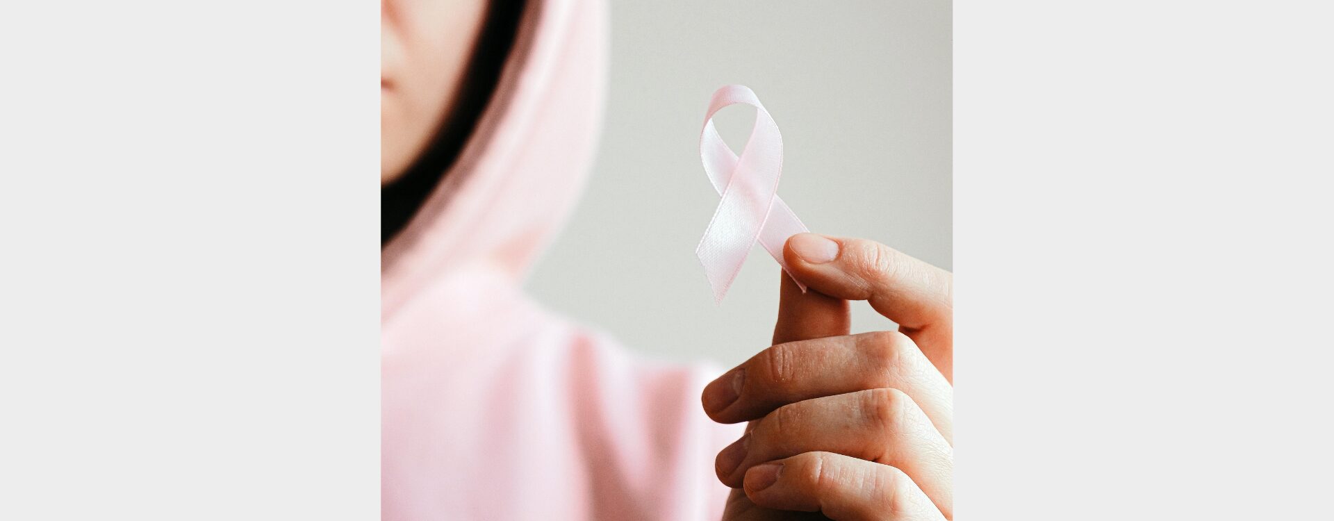 Person in rosa Hoodie hält eine rosa Schleife in der Hand welche für Krebs-Awareness steht