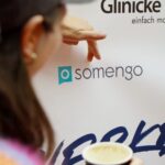 Frau zeigt mir ihren Fingern auf das Somengo-Logo einer Sponsoring-Wand